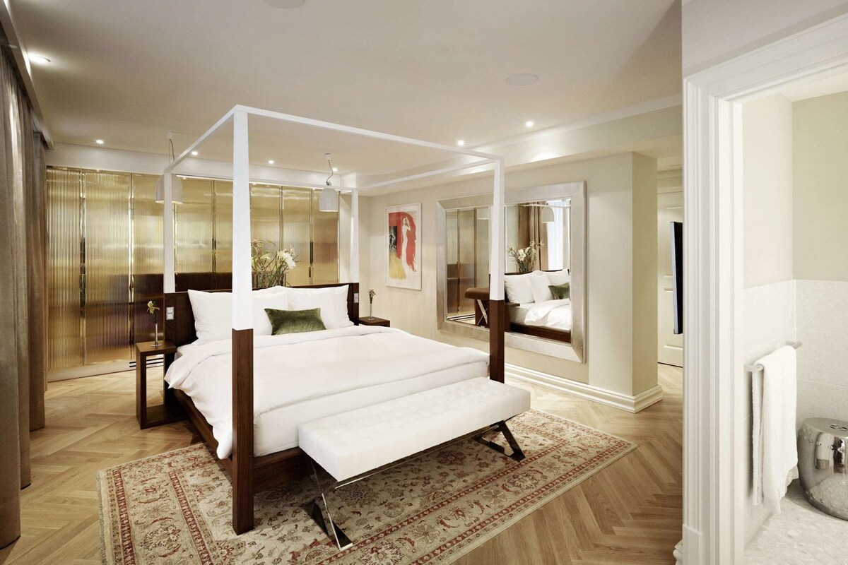 A spacious bedroom with a four-poster bed, a large mirror, and a view of a balcony.
