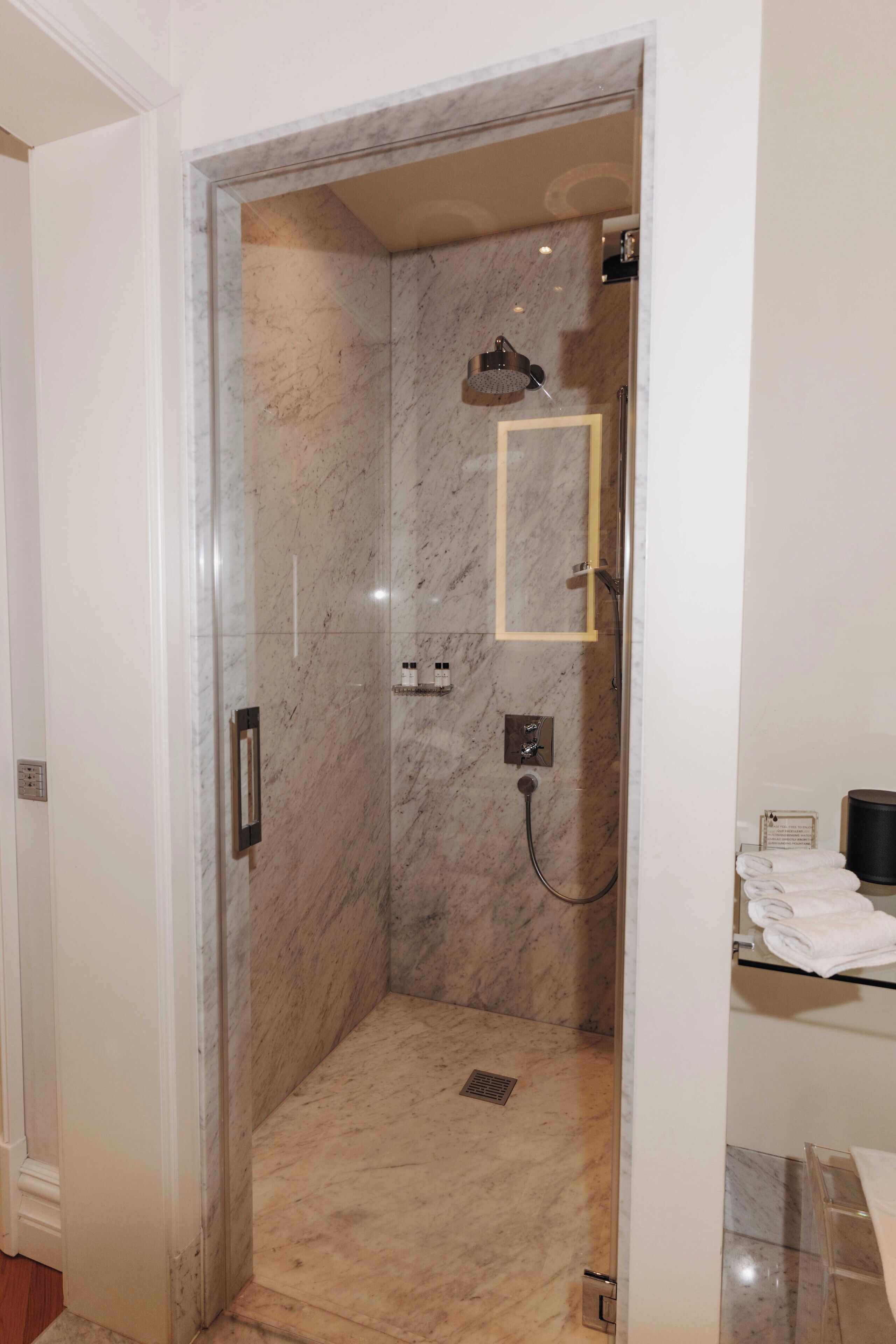 A walk-in shower with a marble wall, a glass door, and a towel rack with folded towels.