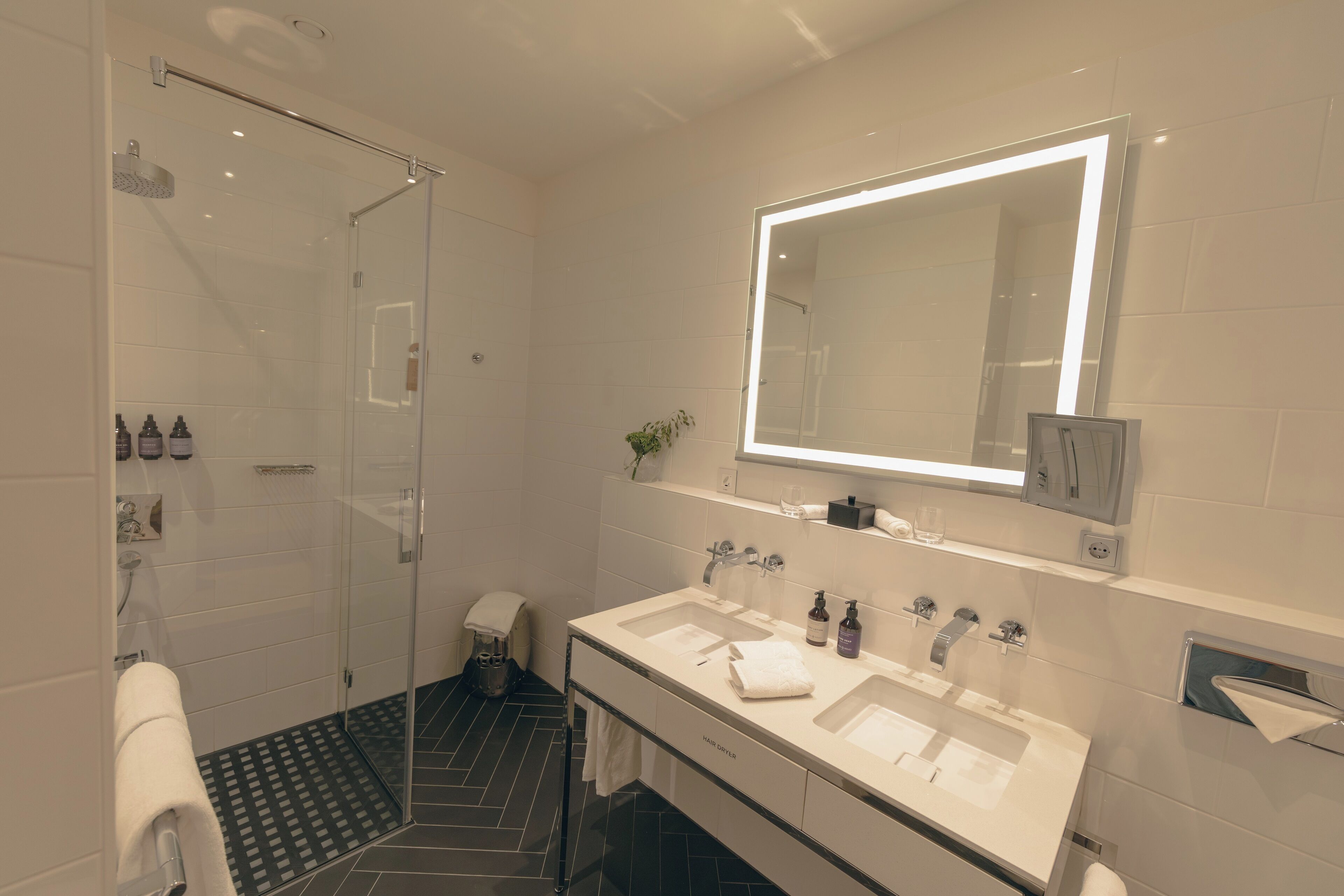 A modern bathroom with a glass-enclosed shower, a large mirror, and dual sinks.