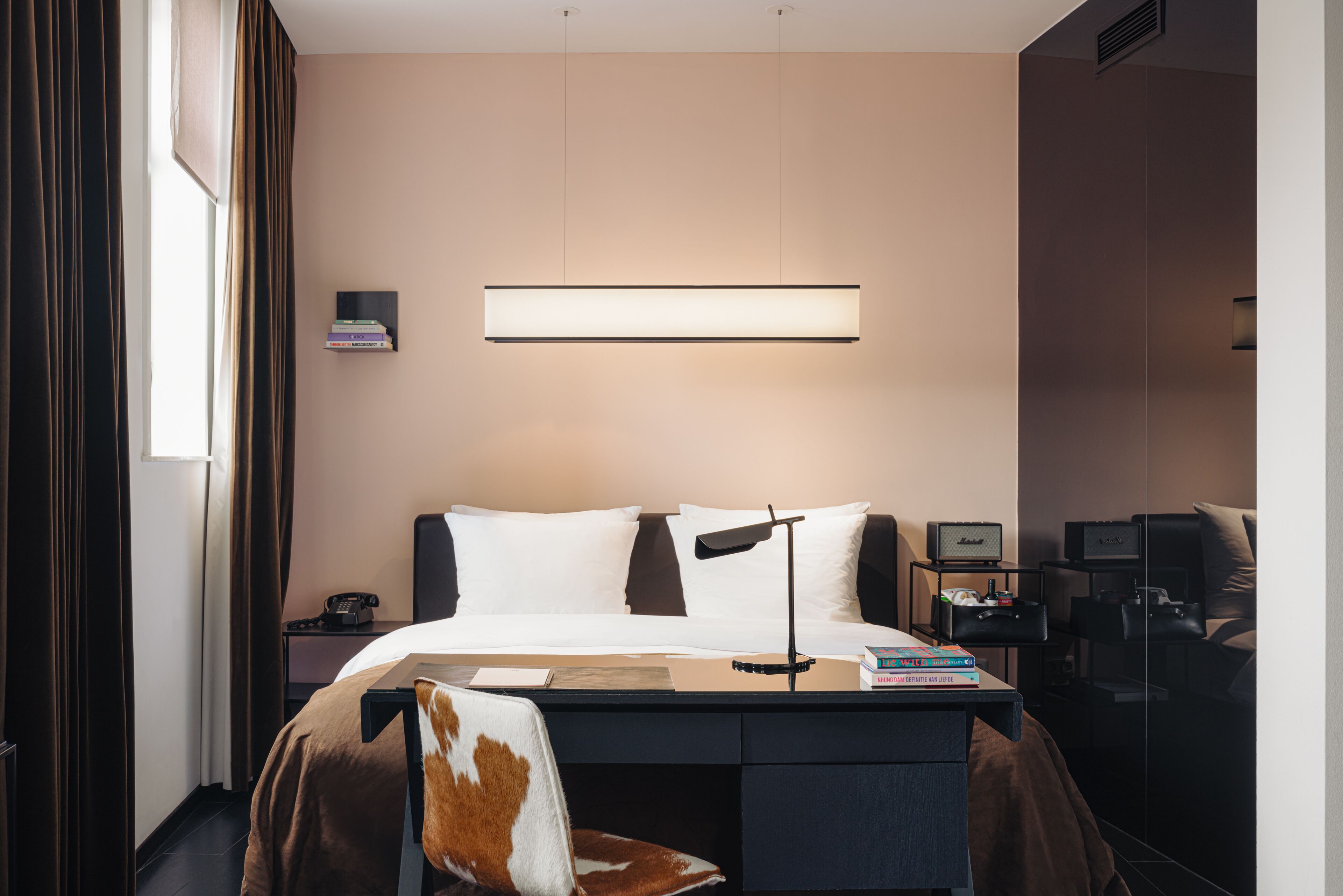 Una habitación de hotel moderna con cama, escritorio, silla y mesita de noche con lámpara y libros.