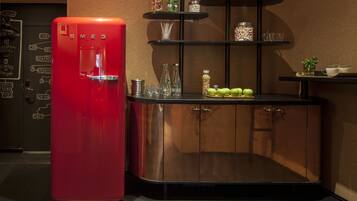 A red refrigerator next to a black cabinet with shelves containing jars and glasses.