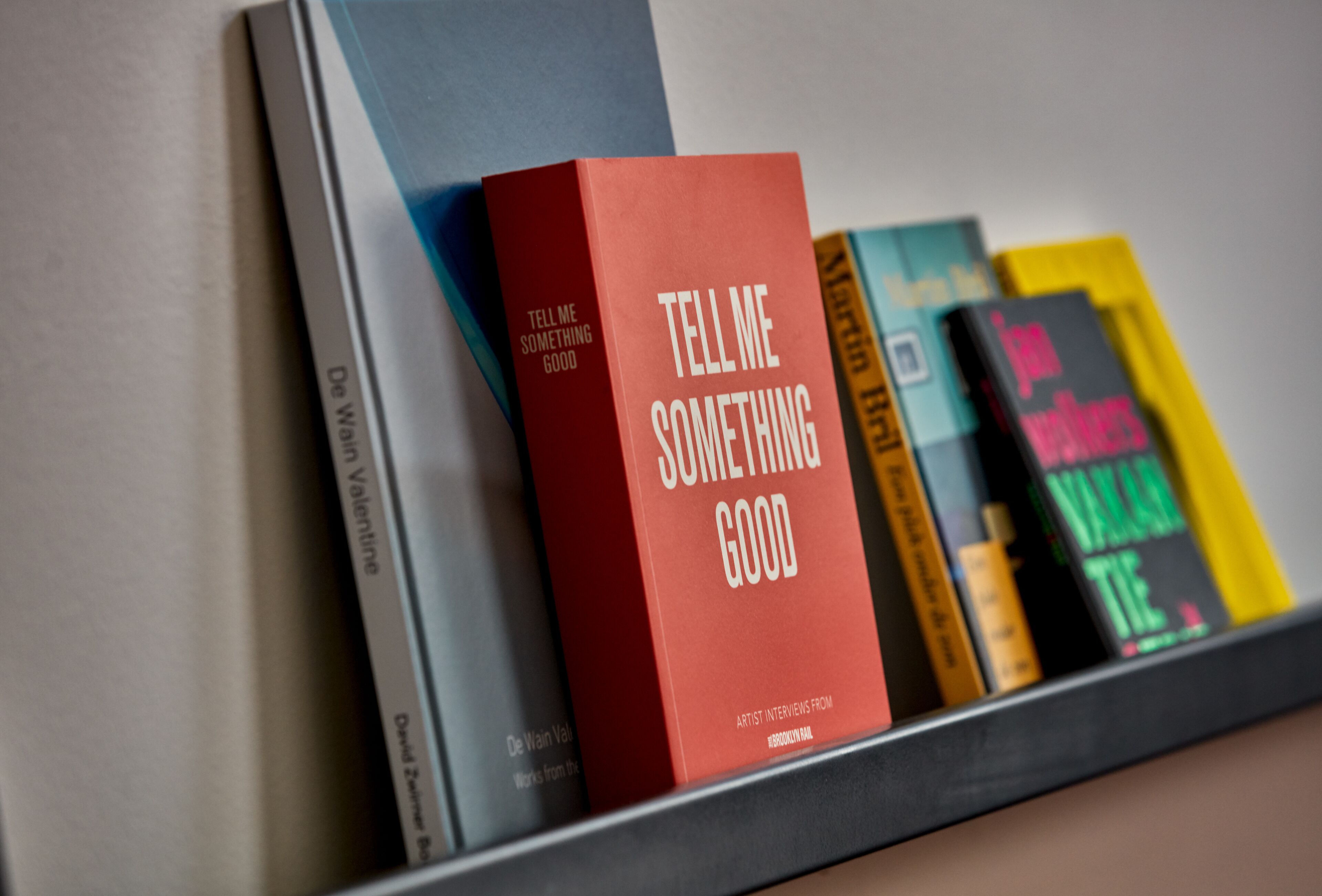 A bookshelf with various books, including a prominent red book titled "Tell Me Something Good."