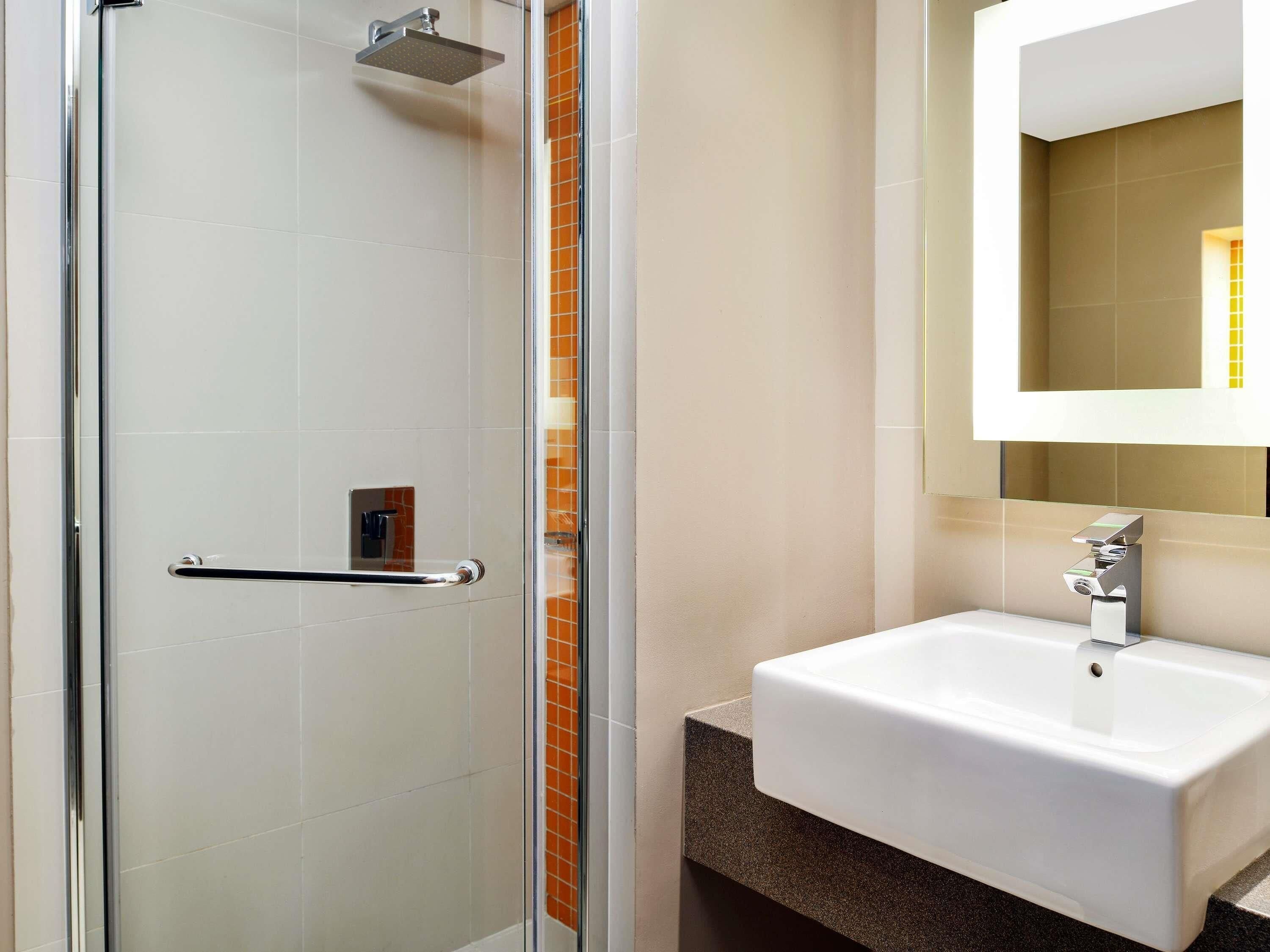 A modern bathroom with a glass shower enclosure, a white sink, and a mirror above the sink.