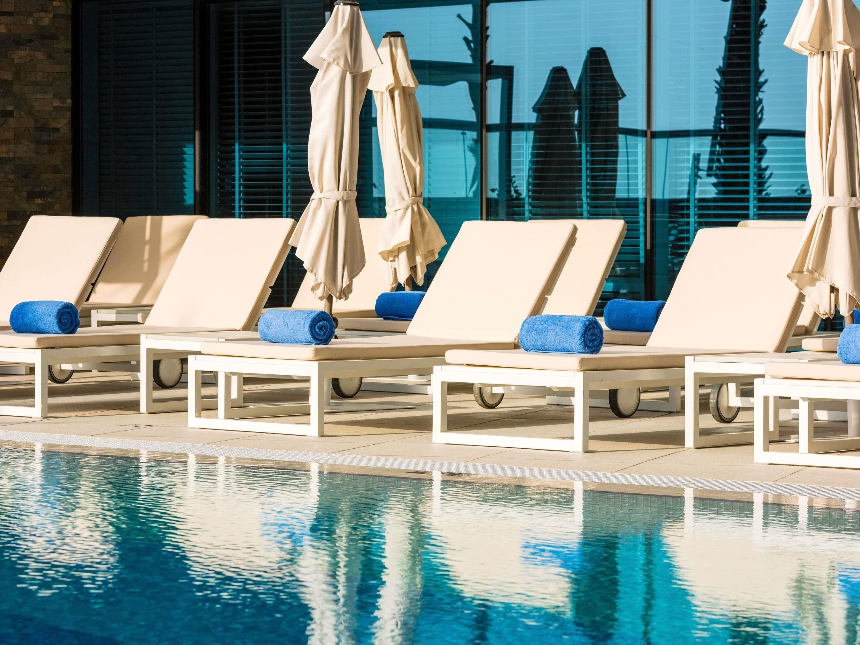 A poolside area with lounge chairs and umbrellas, a clear pool, and a building with large windows in the background.
