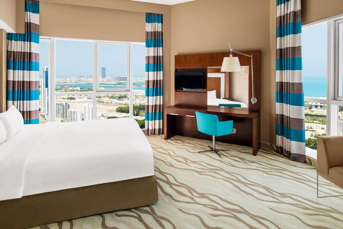 Une chambre d’hôtel équipée d’un lit, d’un bureau, d’une chaise et de grandes fenêtres donnant sur la ville.