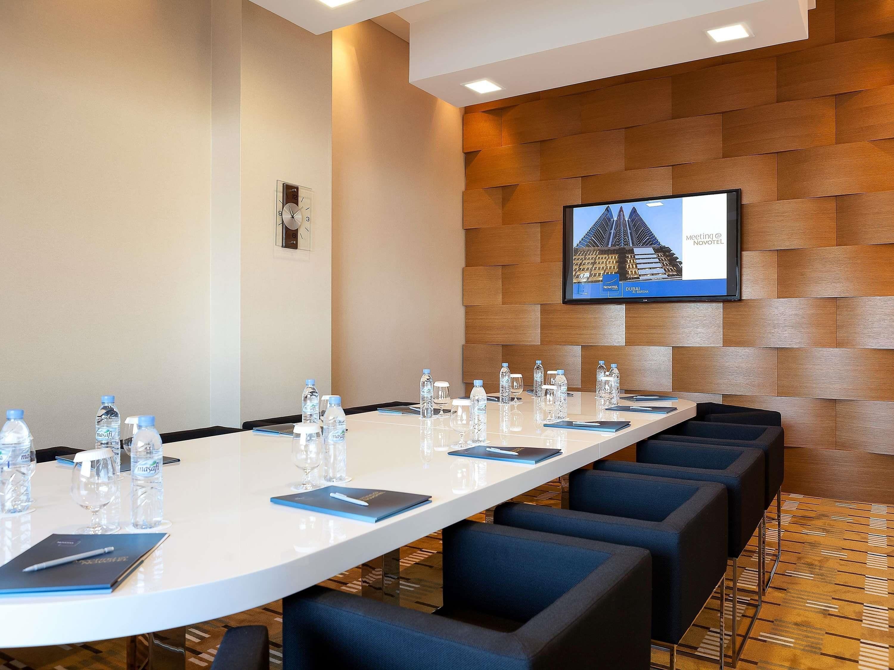 A conference room with a long table, water bottles, glasses, and a TV screen displaying a building.