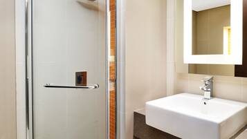 A modern bathroom with a glass shower enclosure, a white sink, and a mirror above it.