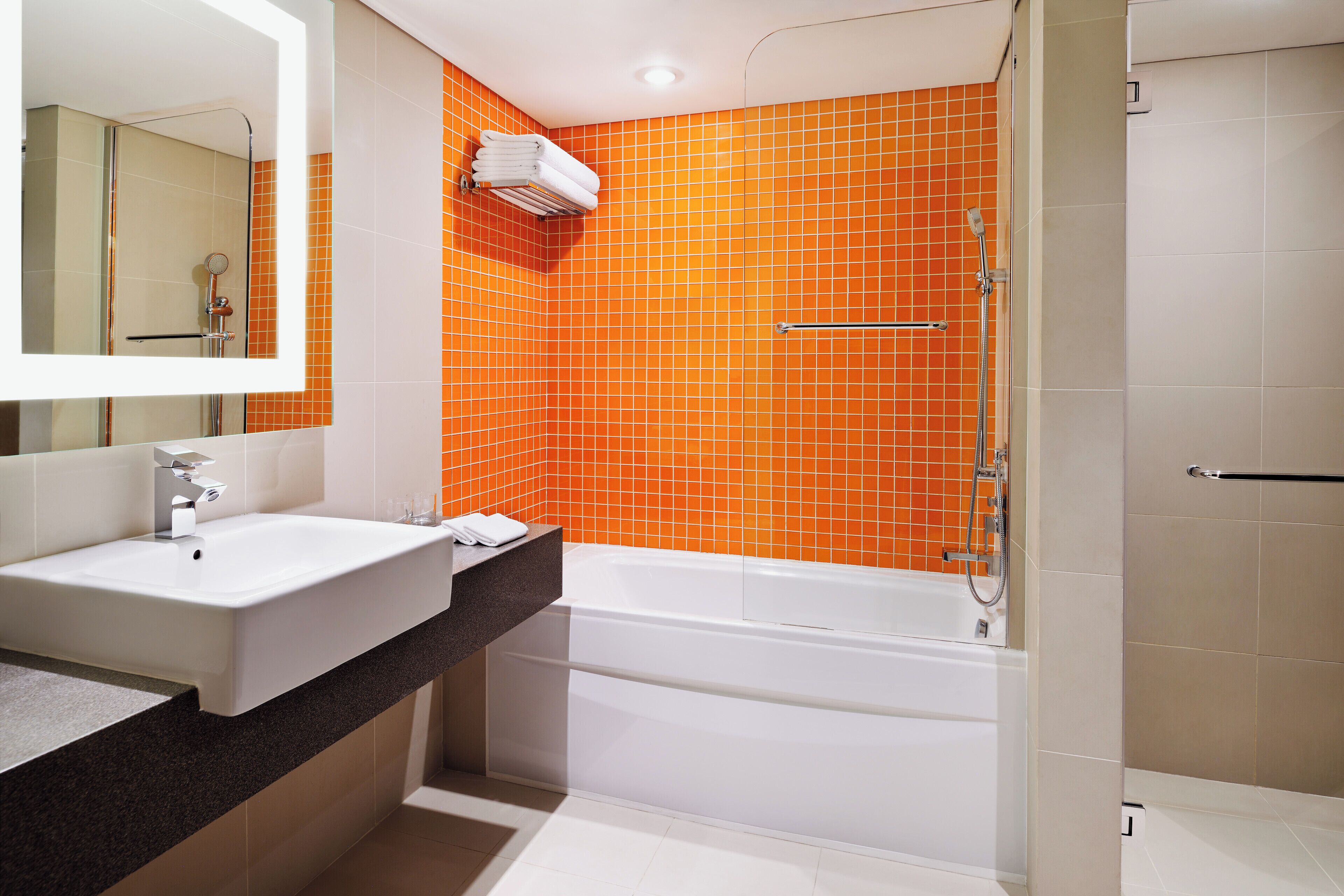 A bathroom with a white sink, a mirror, an orange-tiled shower wall, and a white bathtub.