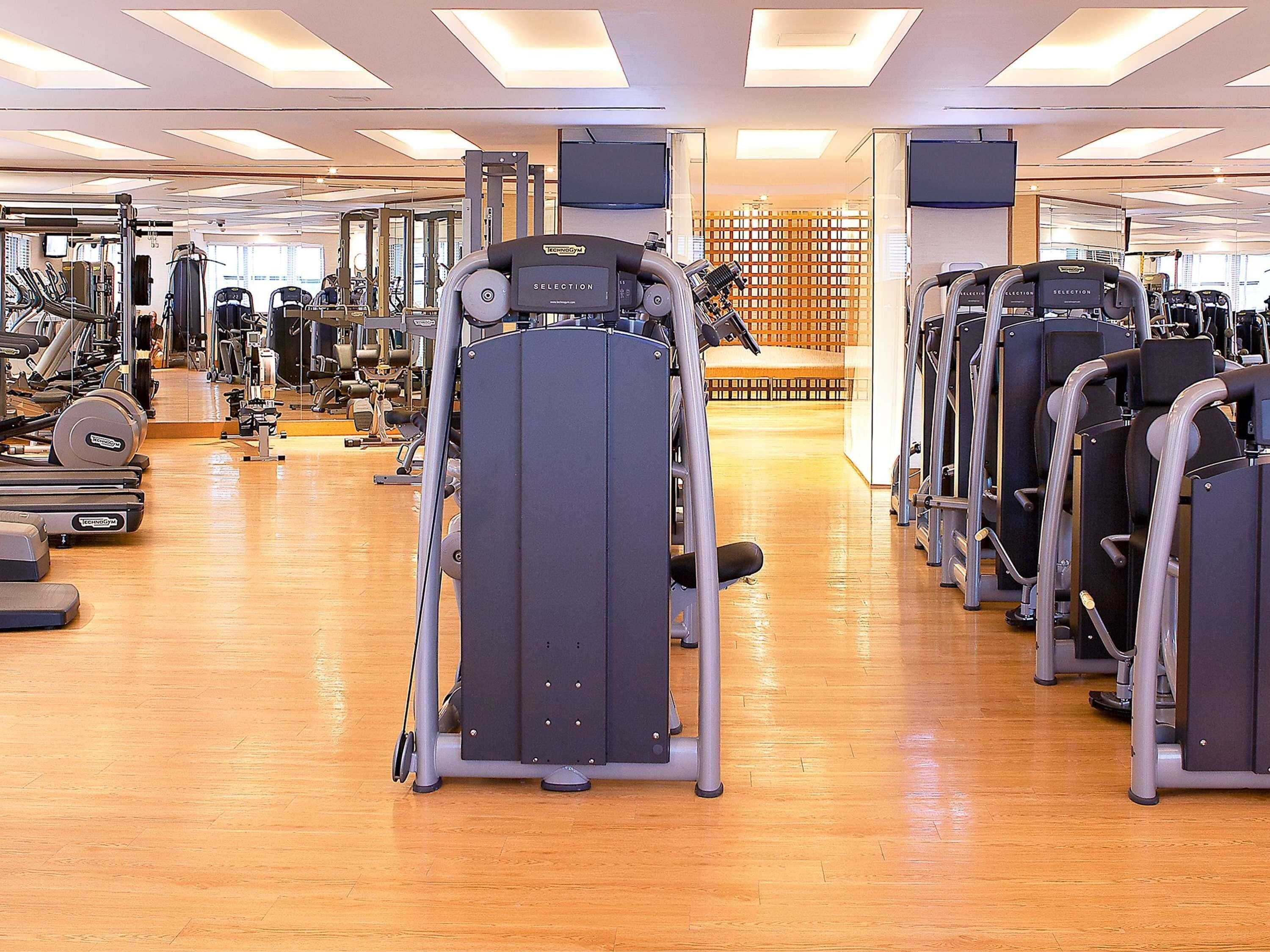 Un gimnasio con diversas máquinas de ejercicio, suelo de madera y luces en el techo.