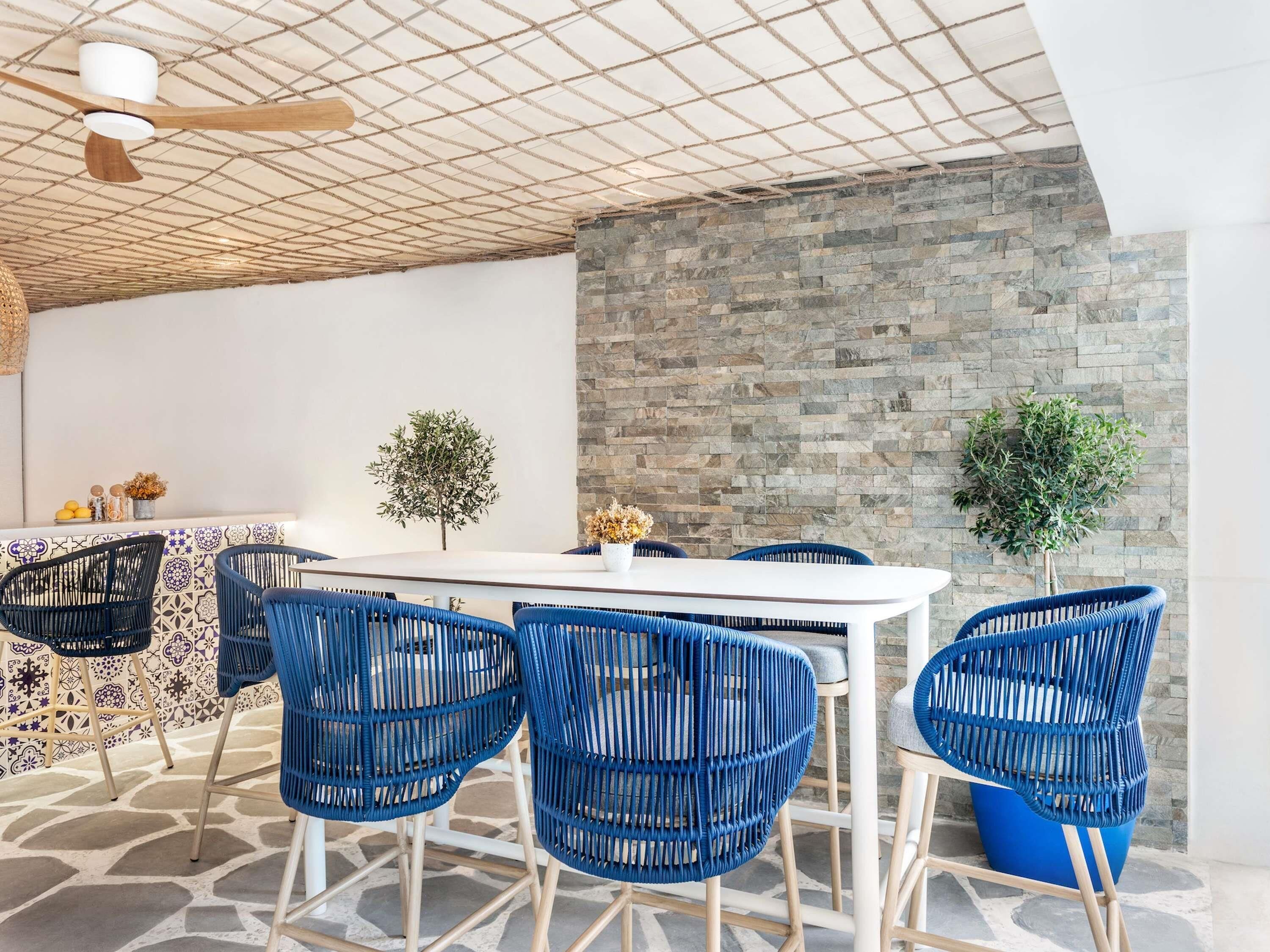 Un comedor con una mesa blanca, sillas azules, una pared de piedra y un ventilador de techo.