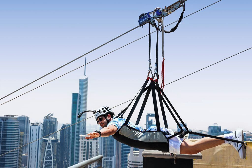 A person in a harness suspended by cables, with a city skyline in the background.