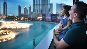 Un hombre sostiene a un niño mientras observan un horizonte urbano con una masa de agua y edificios iluminados.