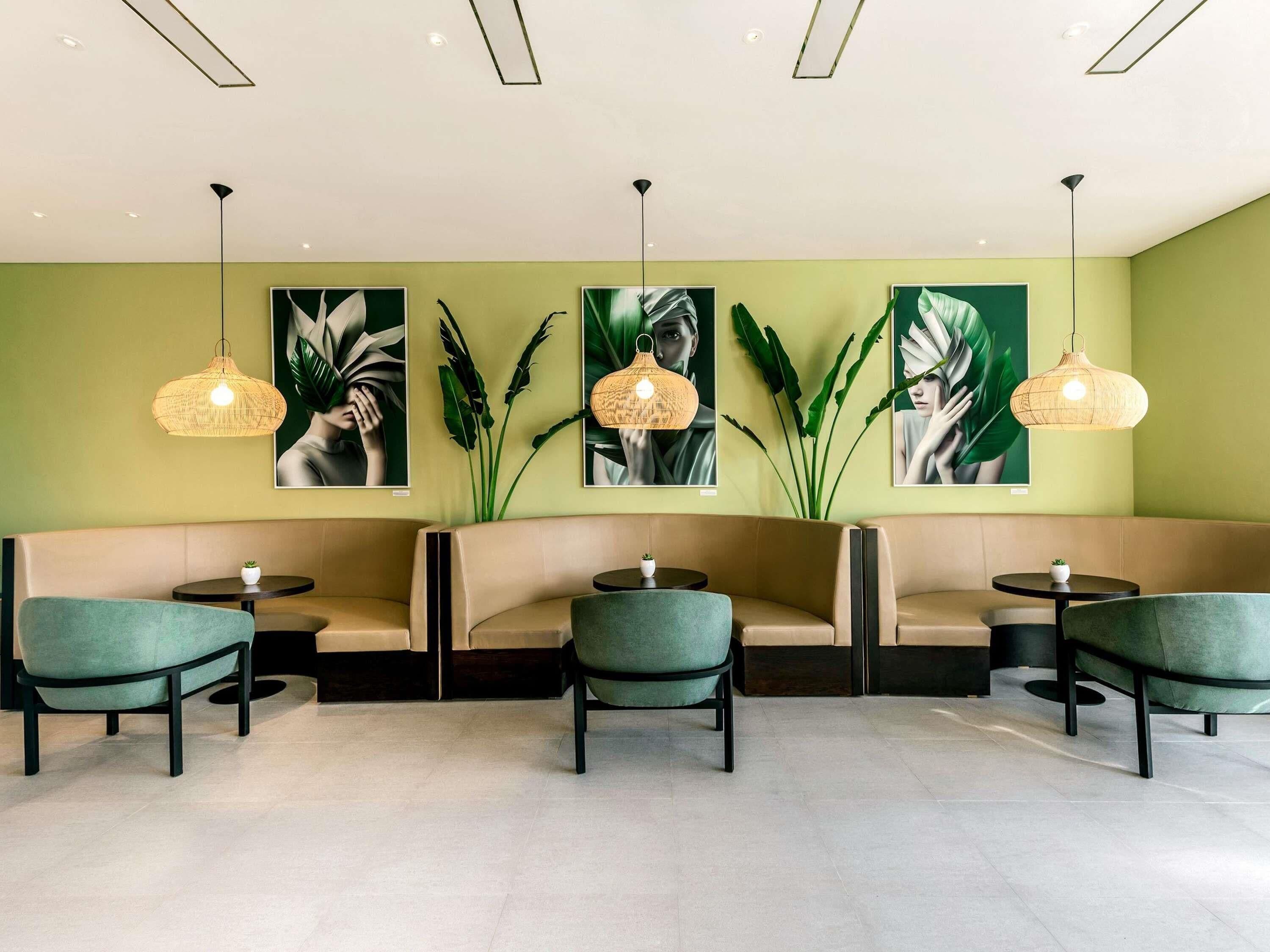 A modern lounge area with green walls, a sofa, chairs, and pendant lights.