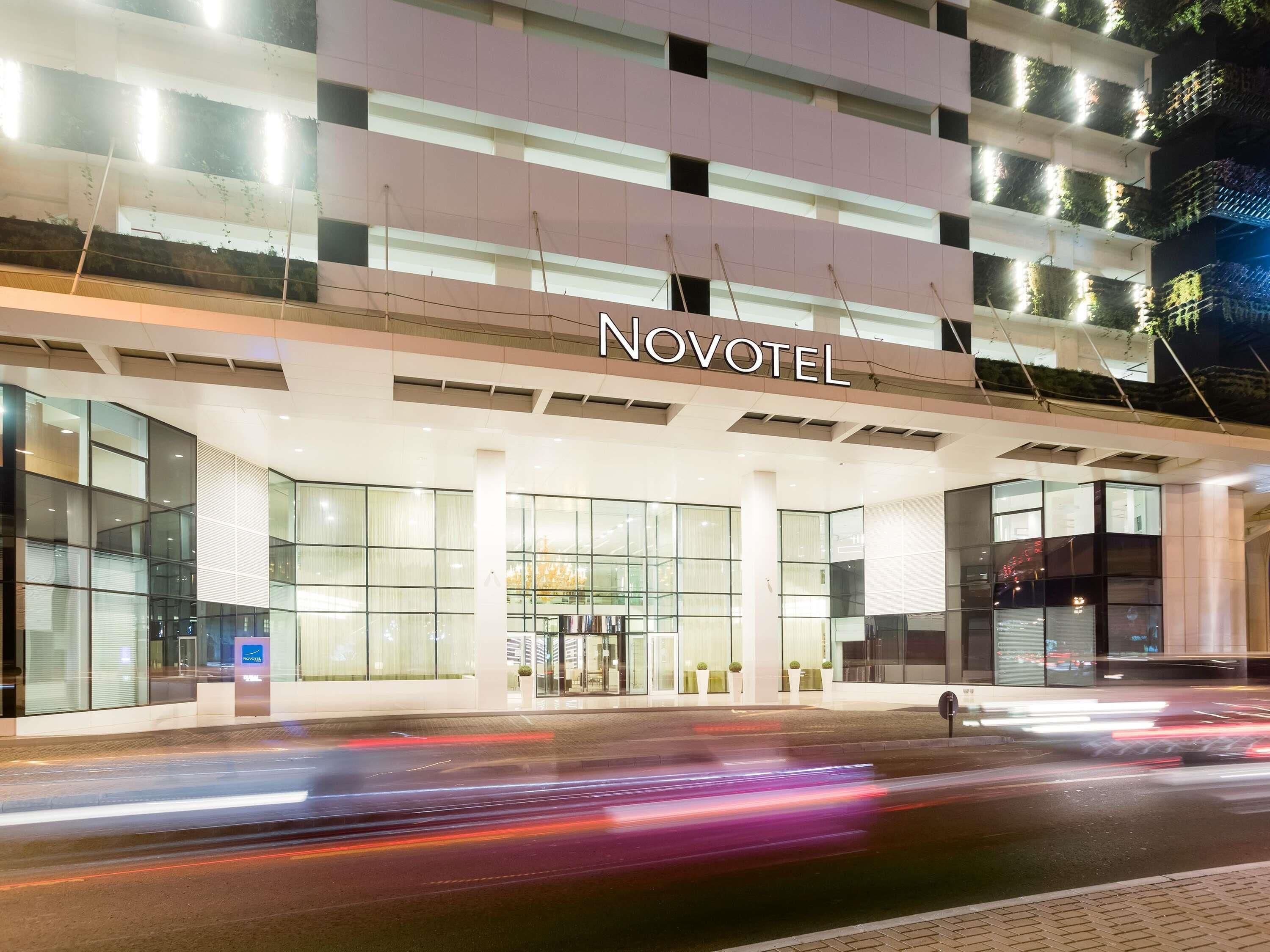 A hotel entrance with a modern design, glass facade, and the name 'NOVOTEL' prominently displayed.