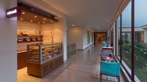 A modern hotel corridor with a bakery display, seating area, and large windows offering views of the outdoors. - Four Points by Sheraton New Delhi, Airport Highway (New Delhi)