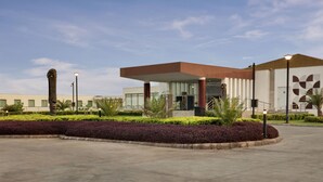 A modern building with a glass entrance, surrounded by landscaped gardens and palm trees. - Four Points by Sheraton New Delhi, Airport Highway (New Delhi)