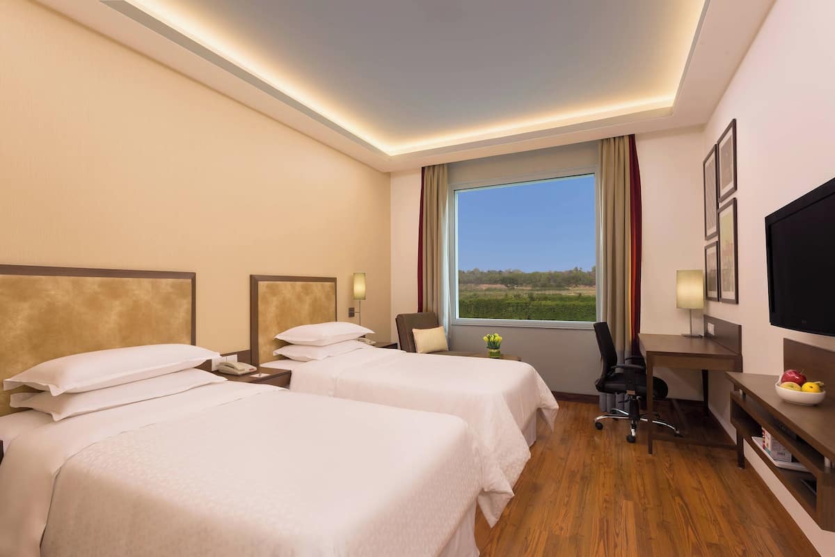 Ein Hotelzimmer mit zwei Betten, einem Schreibtisch, einem Sessel, einem Fernseher und einem Fenster mit Blick ins Freie.