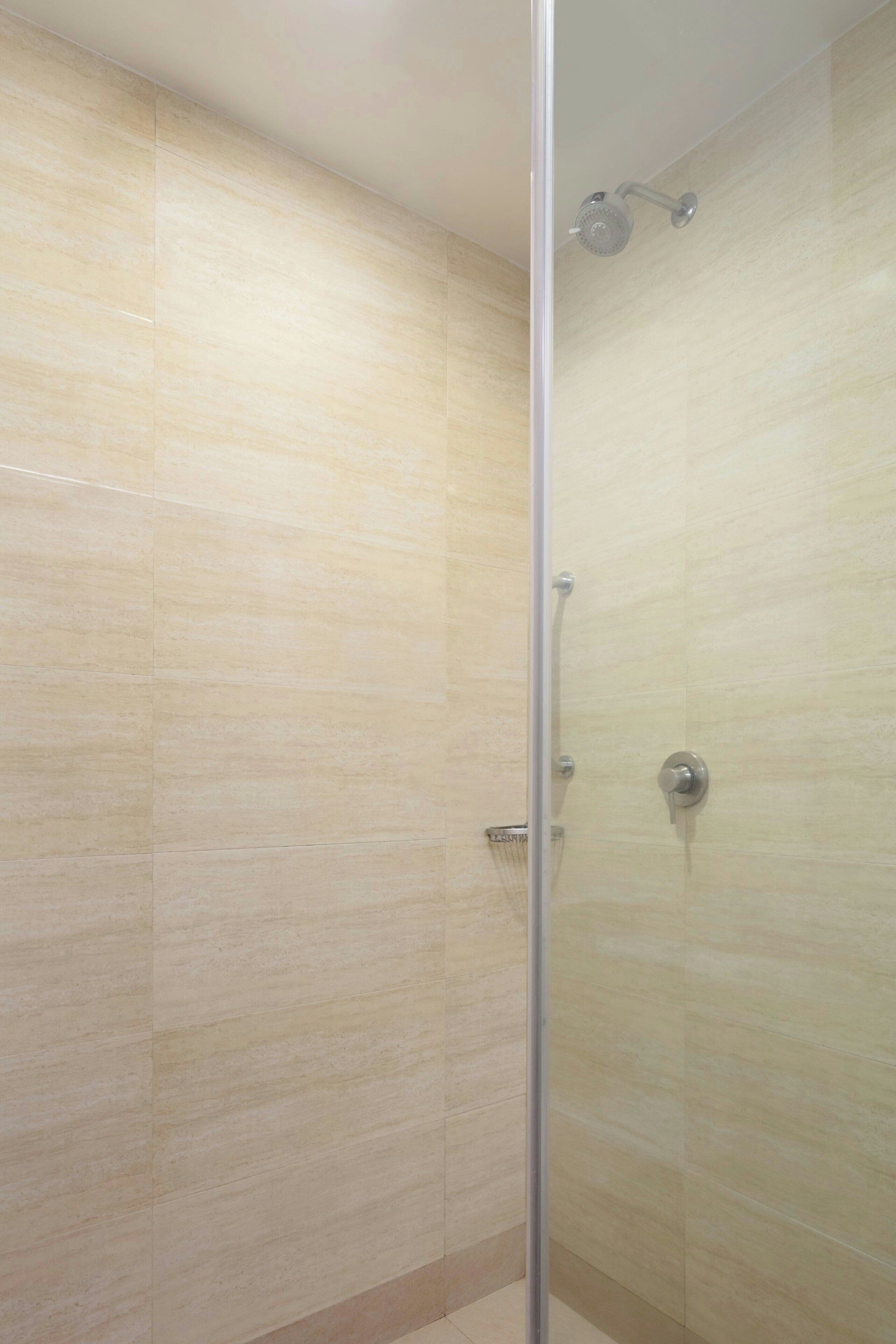 Une douche fermée par des parois en verre, avec des carreaux de couleur beige et une pomme de douche visible.