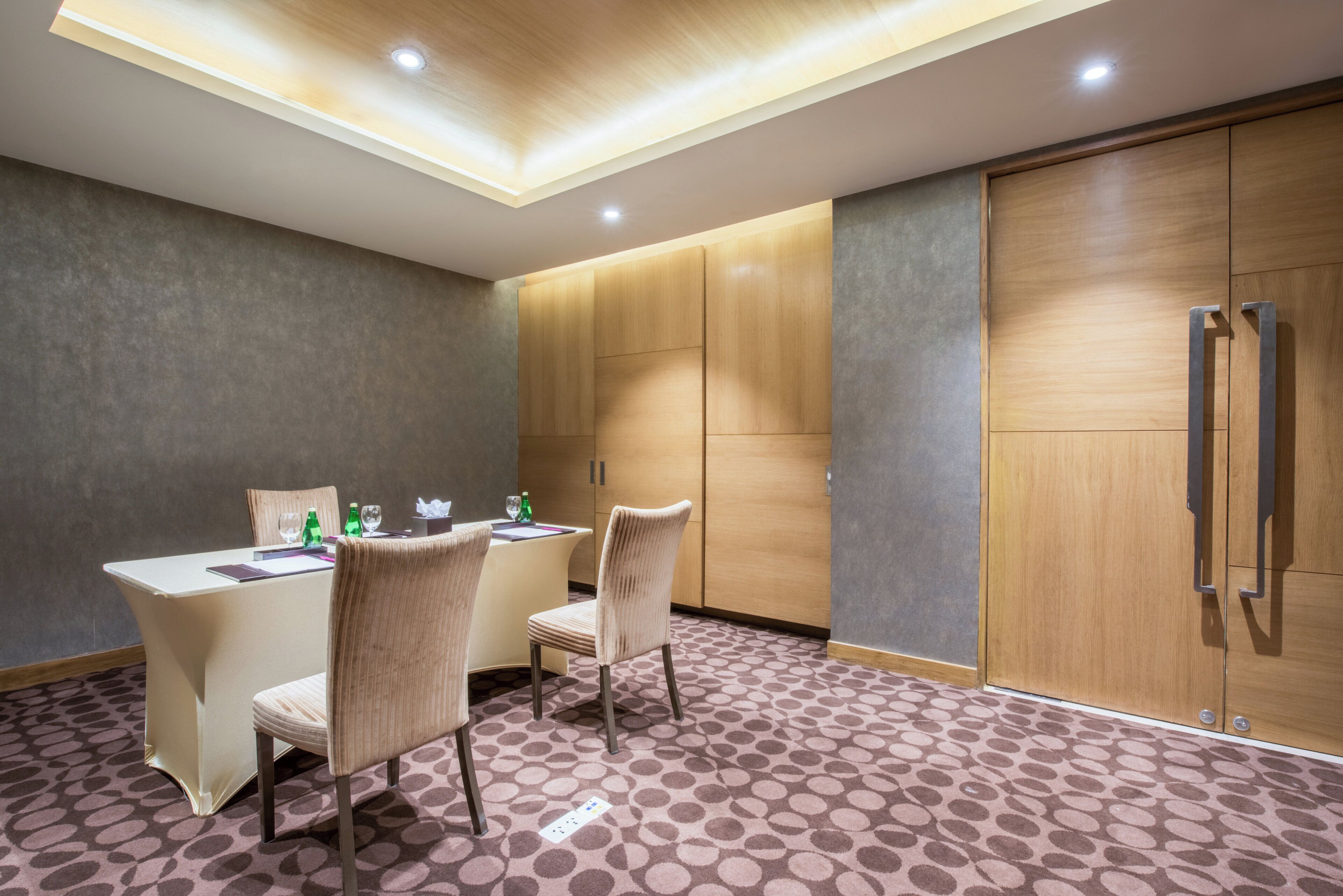 A hotel room with a dining table, two chairs, a minibar, and a wardrobe.