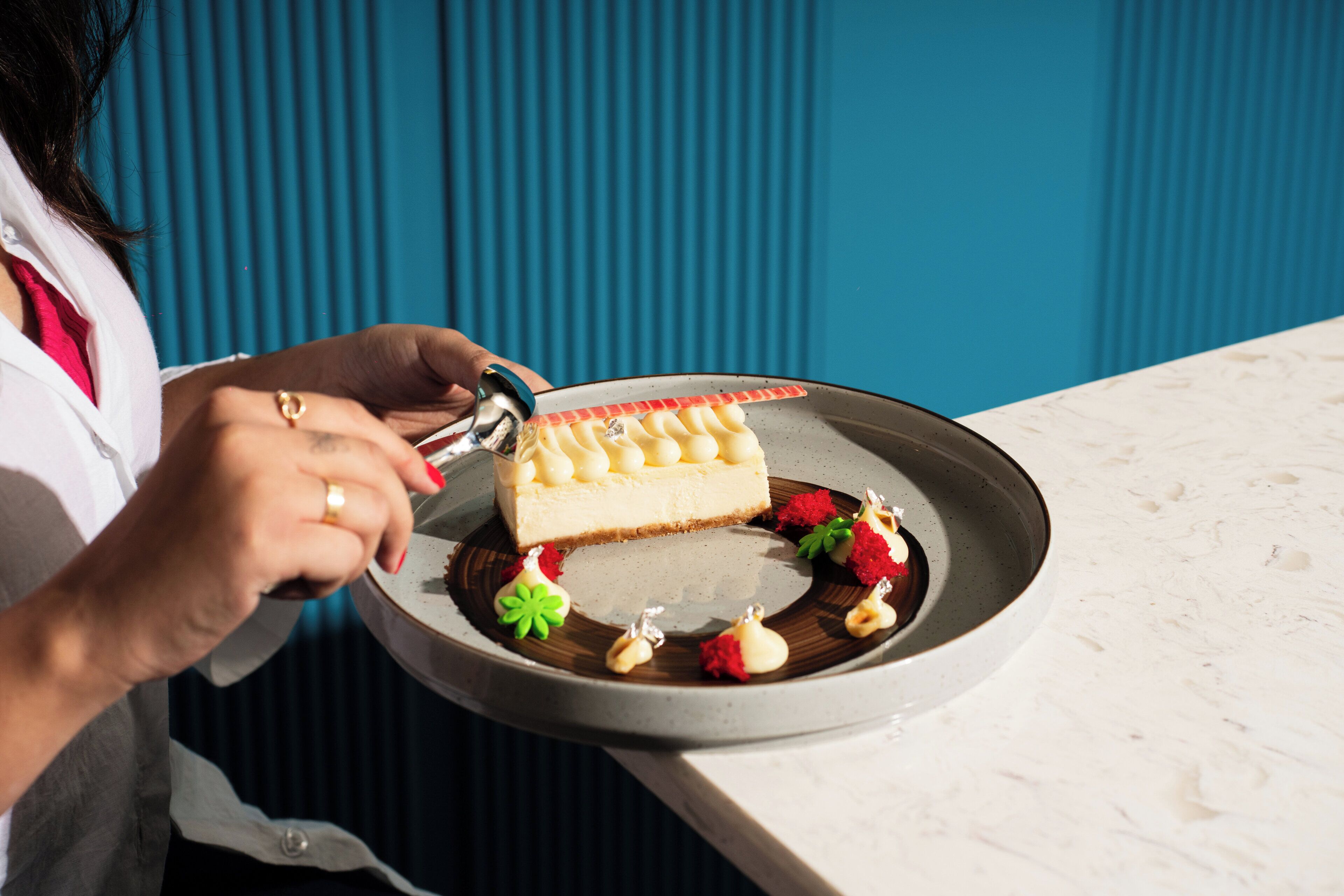 Una persona cortando un pastel de queso en un plato redondo con detalles decorativos.