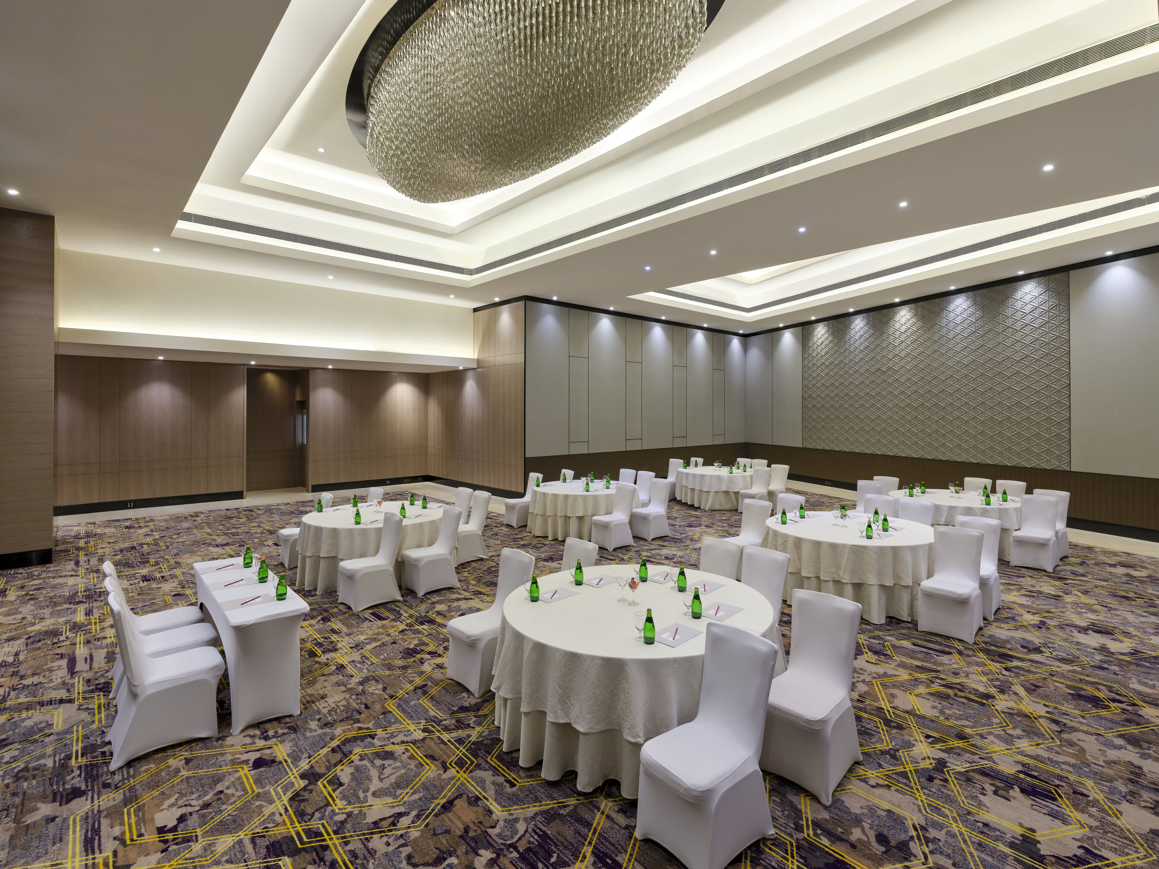 A conference room with multiple round tables, white chairs, and a patterned carpet.
