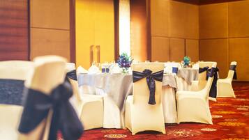 A banquet hall with round tables, white chairs with black sashes, and a red patterned carpet.