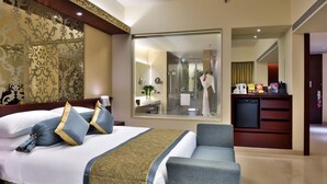A hotel room with a large bed, a sitting area, a bathroom visible through a glass door, and a kitchenette. - Crowne Plaza Ahmedabad City Centre by IHG (Ahmedabad)