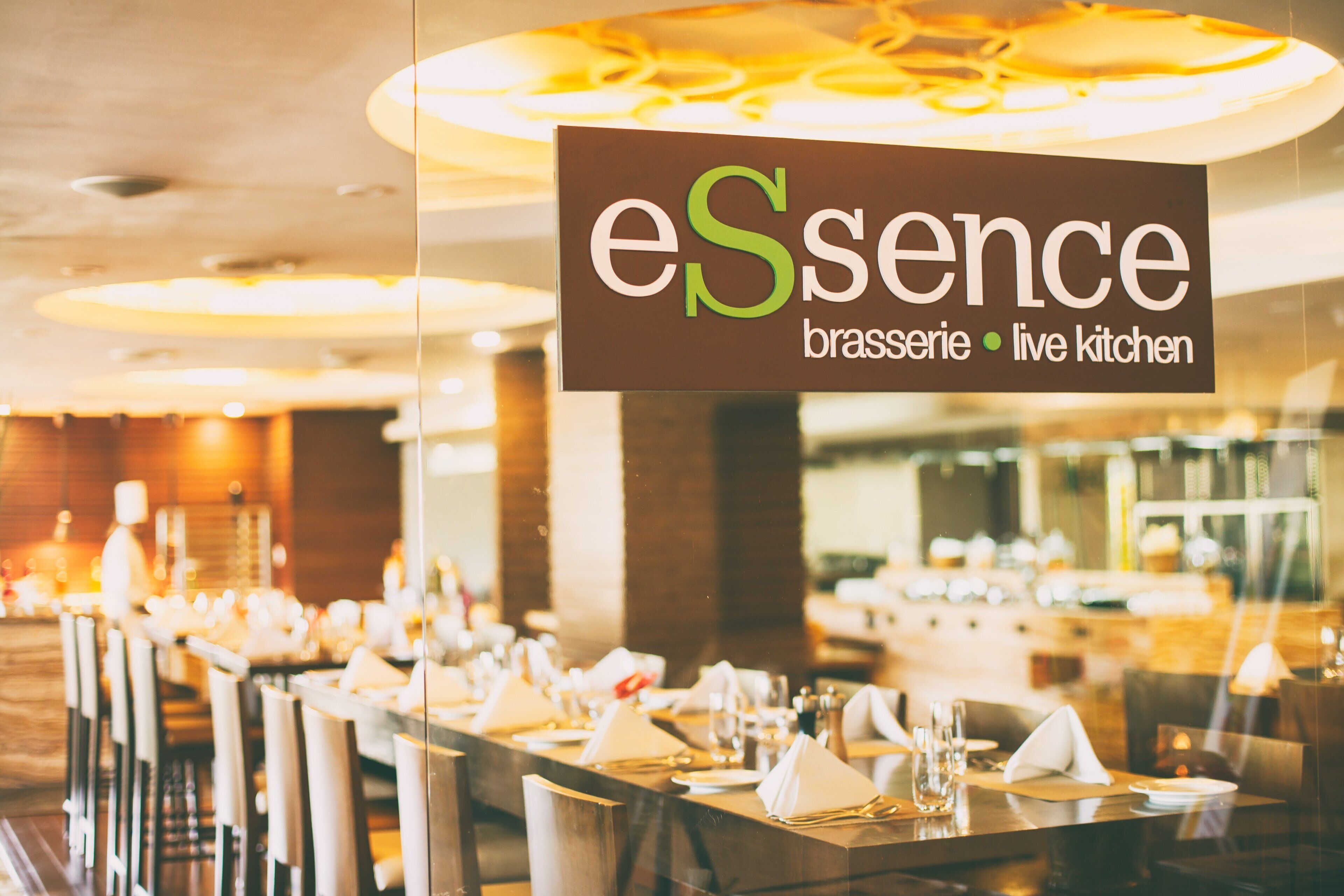 A restaurant interior with tables set for dining, a sign reading "eSence brasserie live kitchen", and a warm, inviting atmosphere.