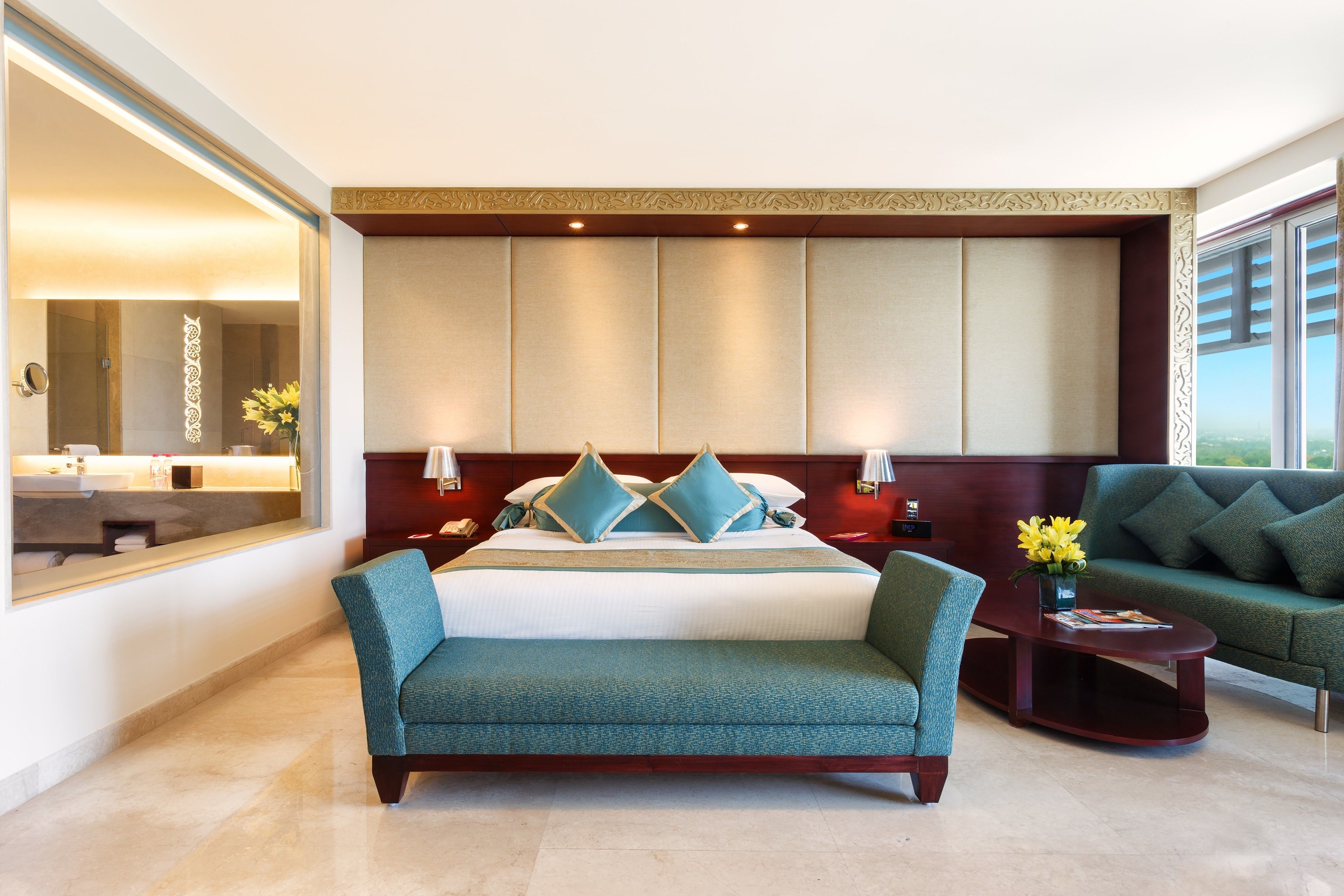 A modern hotel room with a large bed, a sofa, a nightstand, and a mirror.