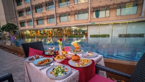 A dining table set with various dishes, a rose, and a cocktail glass by a poolside. - Crowne Plaza Ahmedabad City Centre by IHG (Ahmedabad)