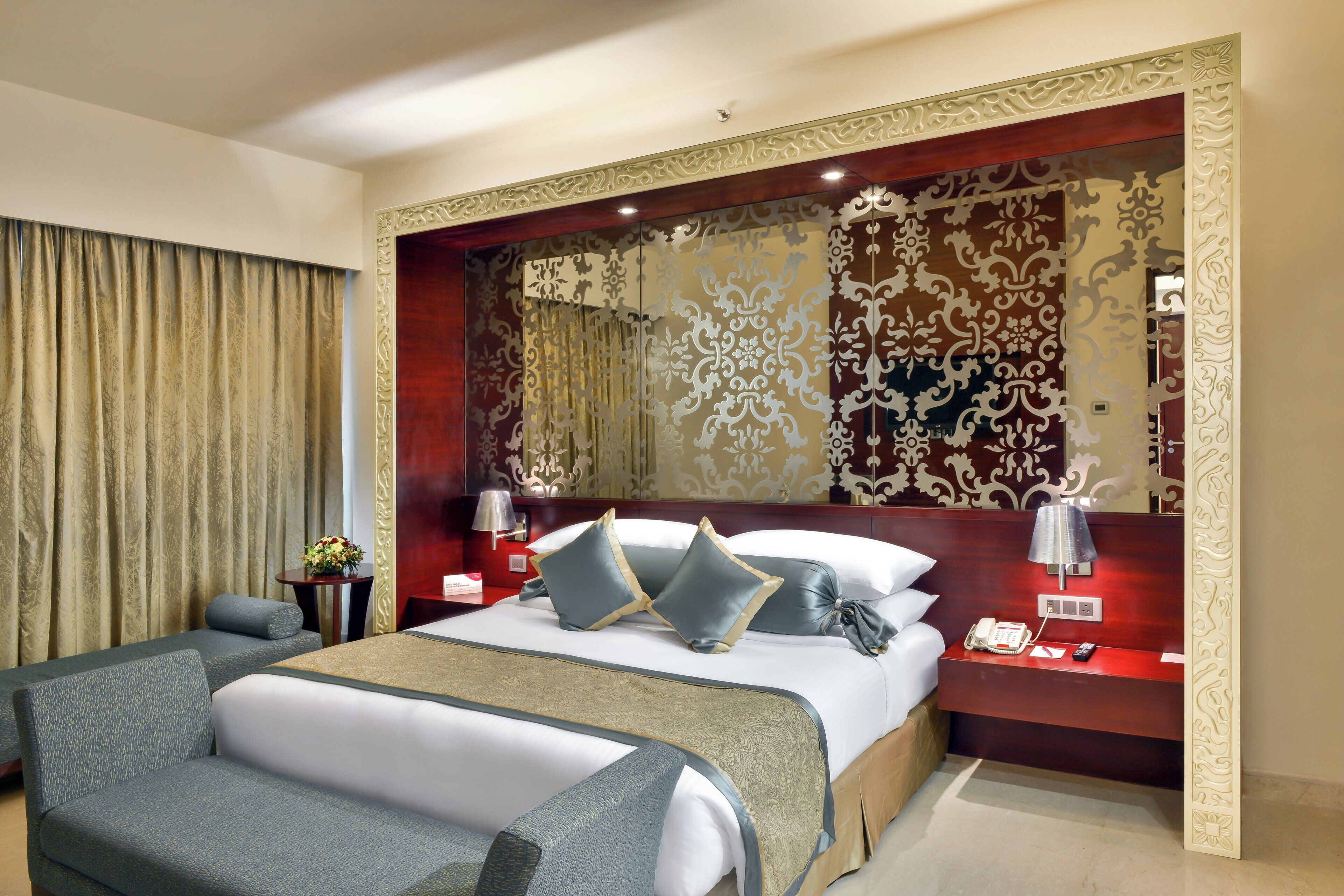 A hotel room with a large bed, a desk, a chair, a lamp, and a telephone.