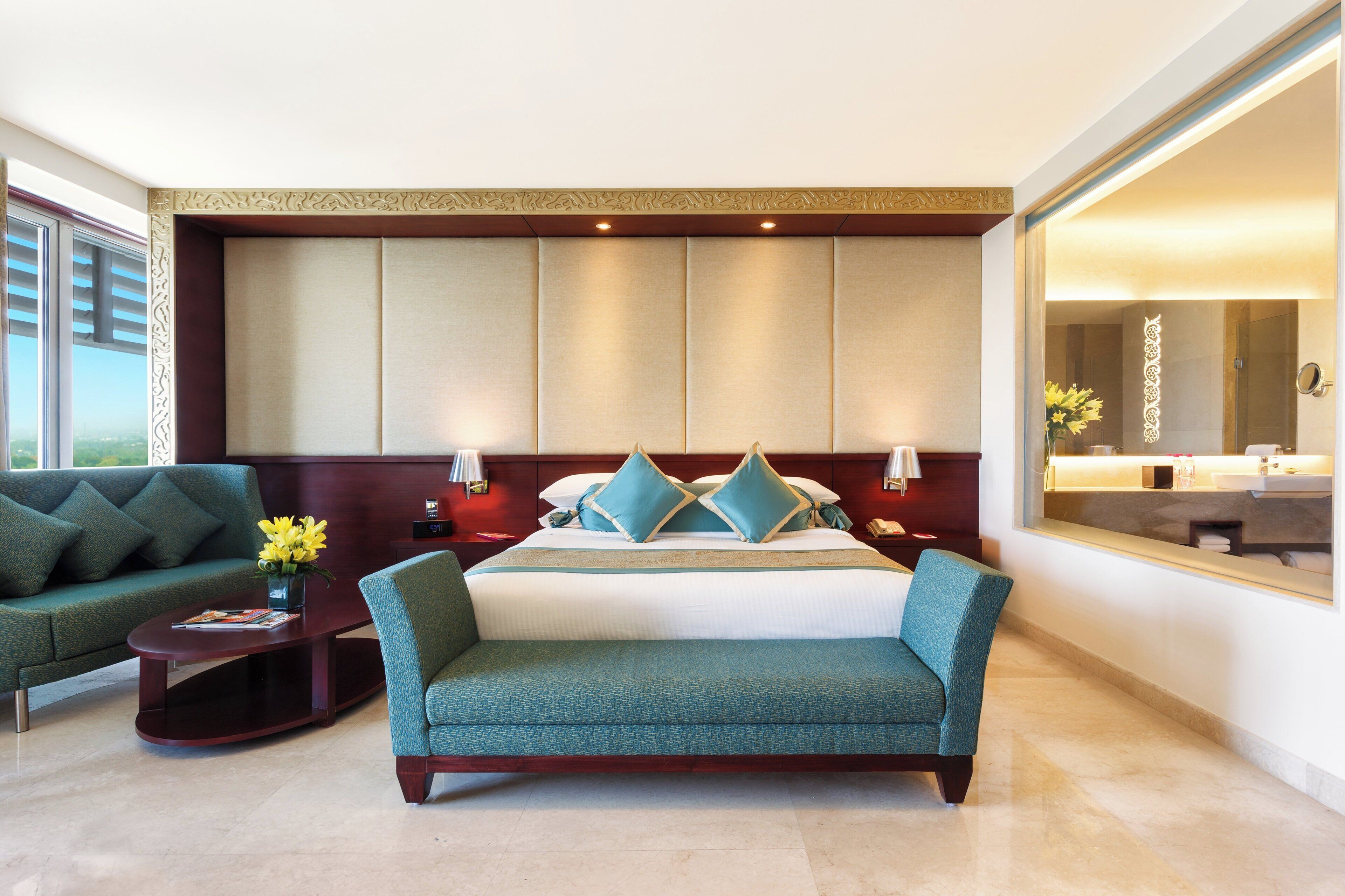 A hotel room with a bed, a sofa, a nightstand, a lamp, and a large mirror.