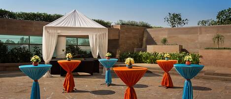 Un patio con un dosel blanco y mesas con cortinas azules y naranjas, cada una con un jarrón de flores.
