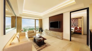 Habitación de hotel moderna con un televisor grande, asientos cómodos, vistas a la ciudad y una zona de dormitorio separada.