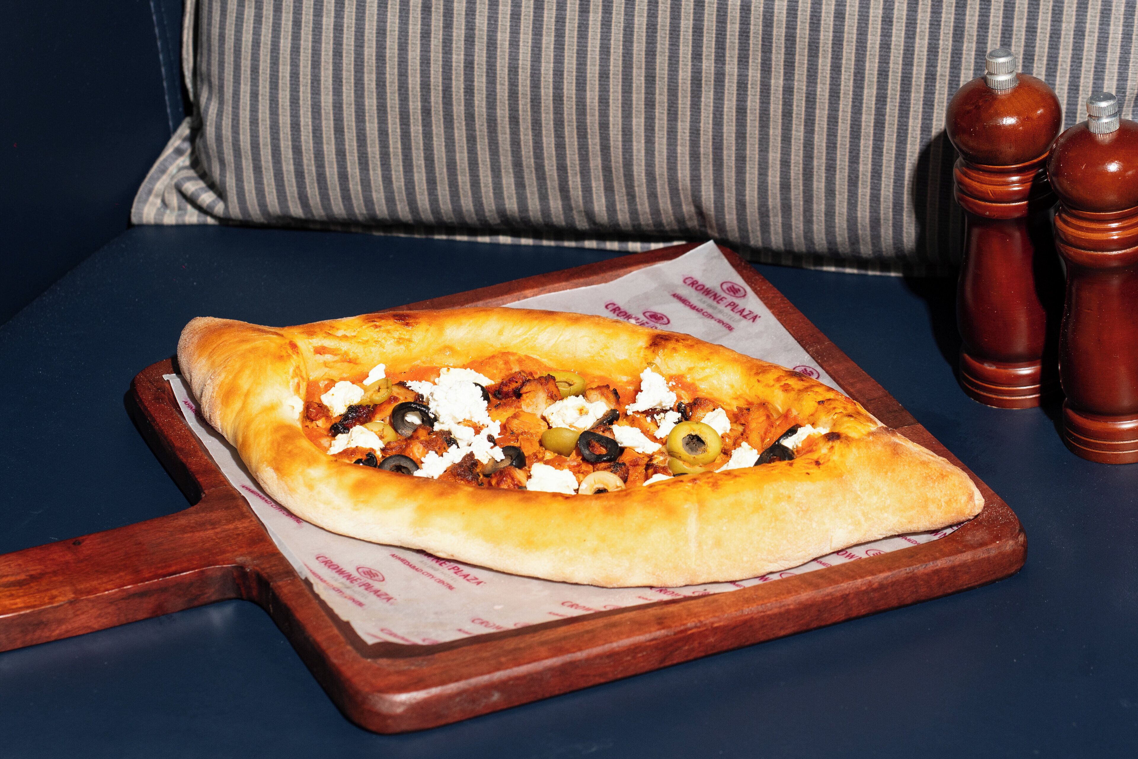 A long bread with toppings, placed on a wooden board on a table.