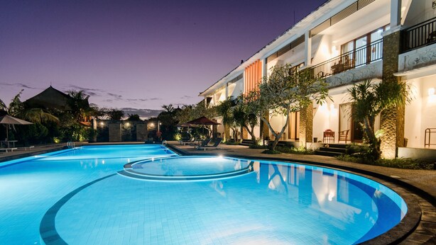 A swimming pool with a circular design, surrounded by a landscaped area with trees and a building with balconies.