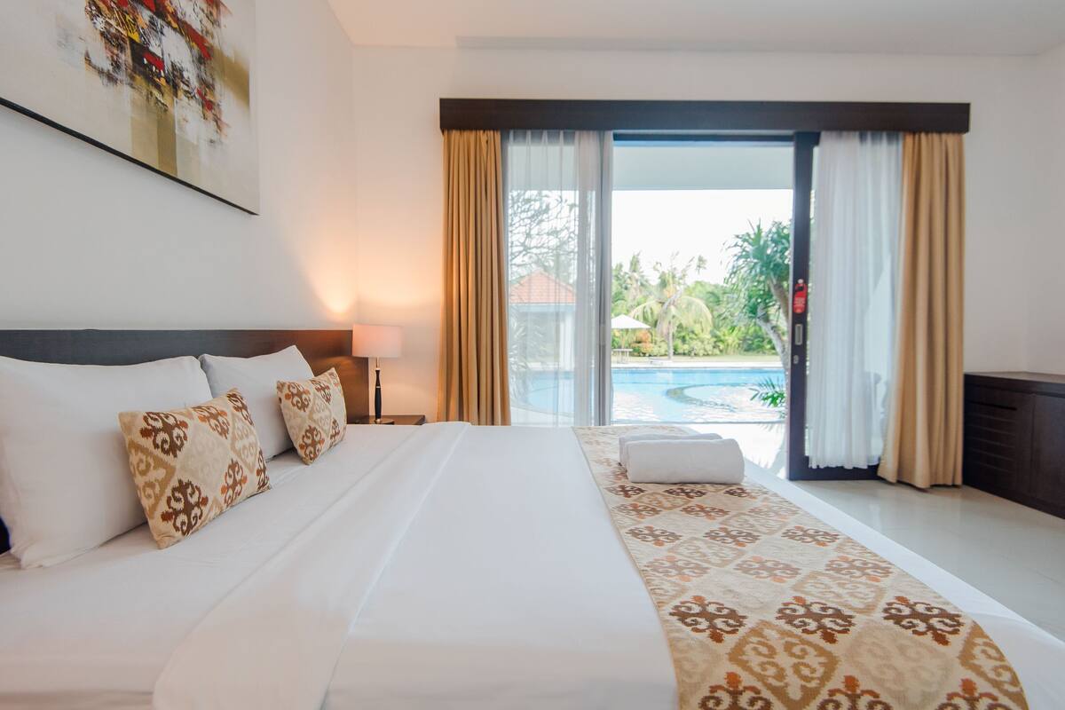 Een hotelkamer met een groot bed, uitzicht op een zwembad en een balkon met gordijnen.