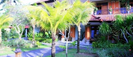 A traditional house with a tiled roof, surrounded by lush greenery including palm trees and other tropical plants.