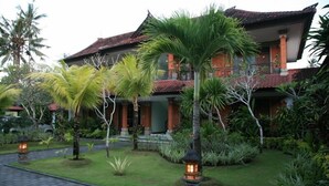 A traditional house with a tiled roof, surrounded by lush greenery and palm trees.