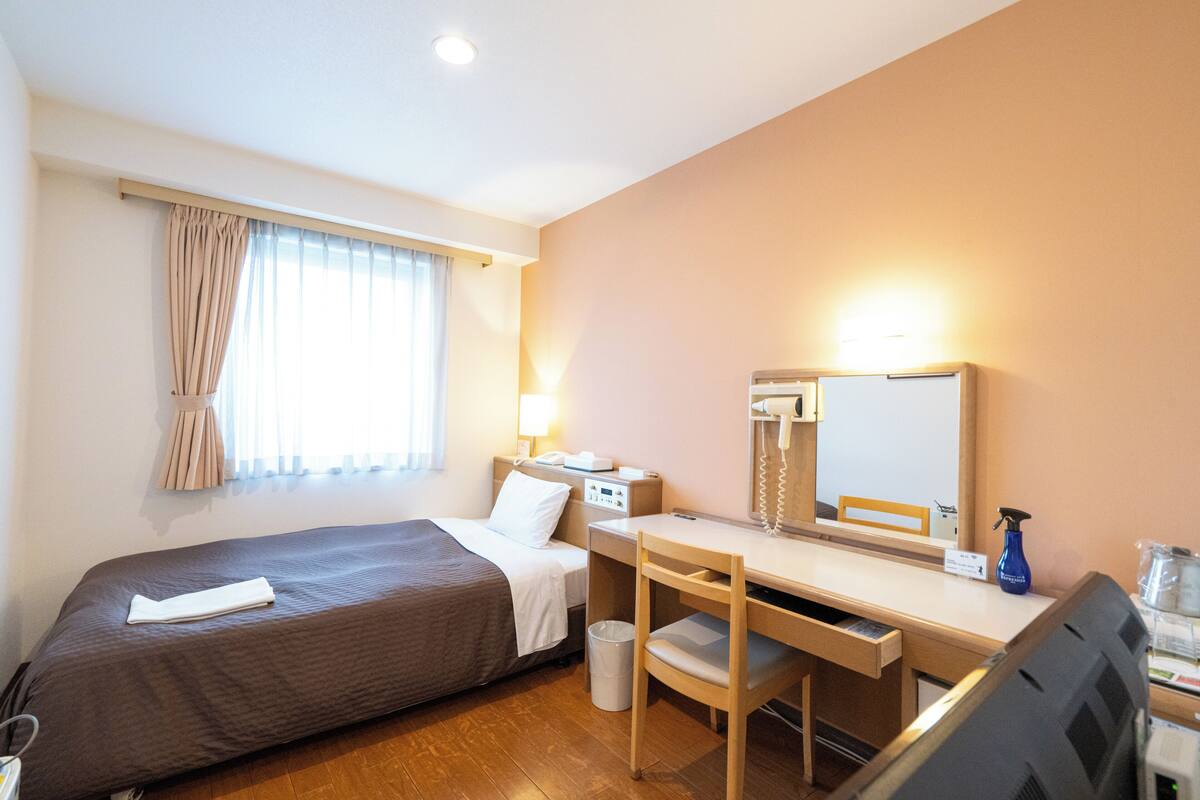 Una habitación de hotel con cama, escritorio, silla y un pequeño cubo de basura.