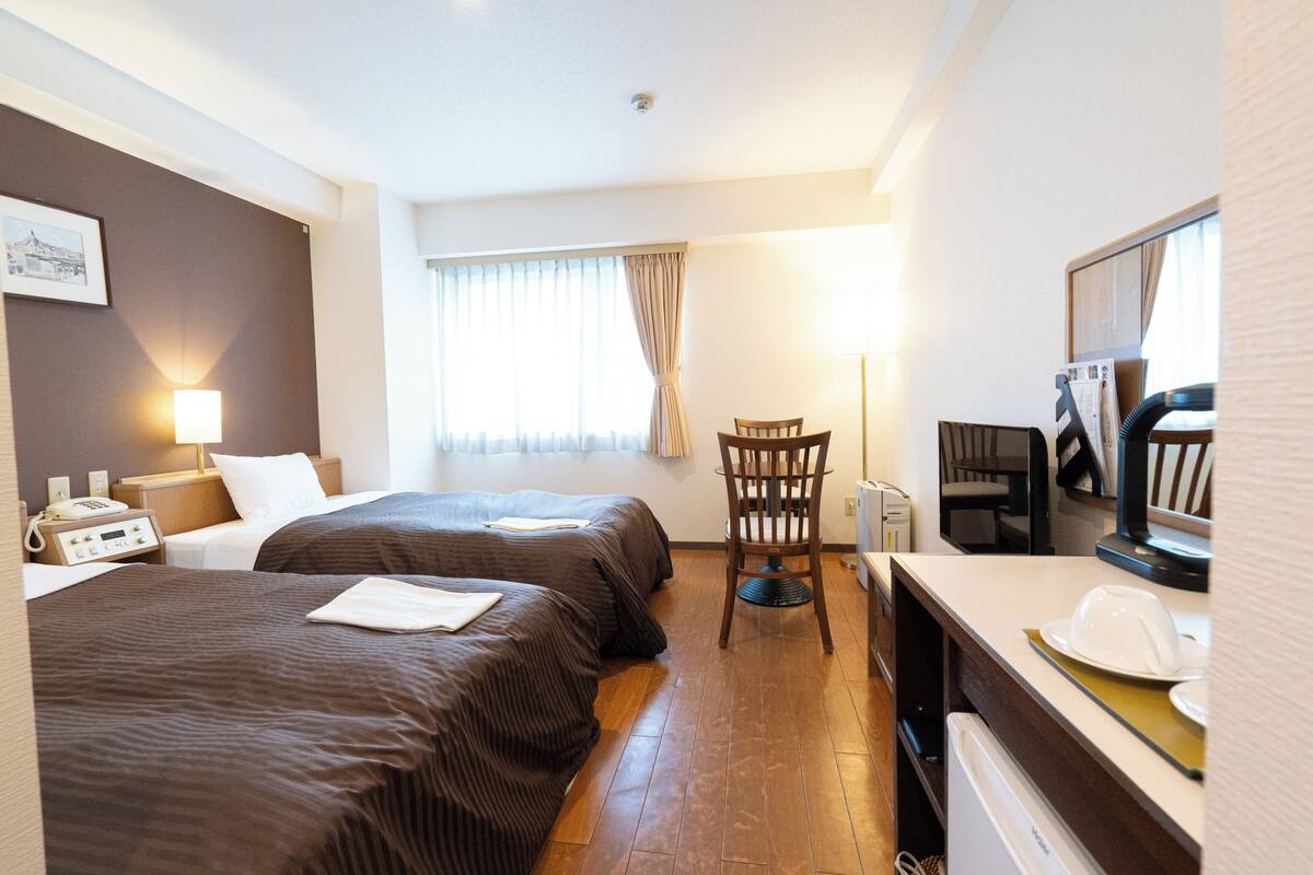 Habitación de hotel con dos camas, un escritorio, una silla, un televisor y una ventana con cortinas.