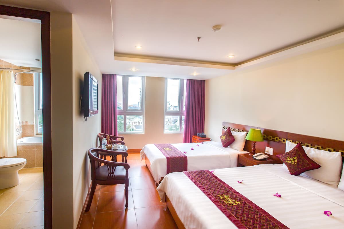A hotel room with two beds, a desk, a chair, a TV, and a bathroom with a toilet and shower.
