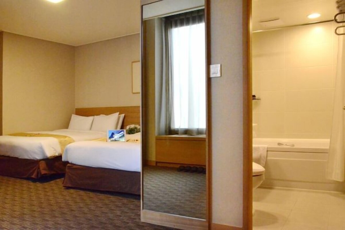 A hotel room with two beds, a bathroom with a bathtub, and a large mirror.