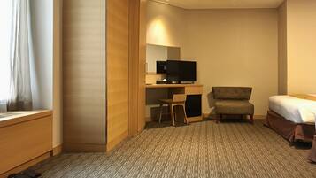 Quarto de hotel com cama, escrivaninha, televisão, cadeira e janela com cortinas.