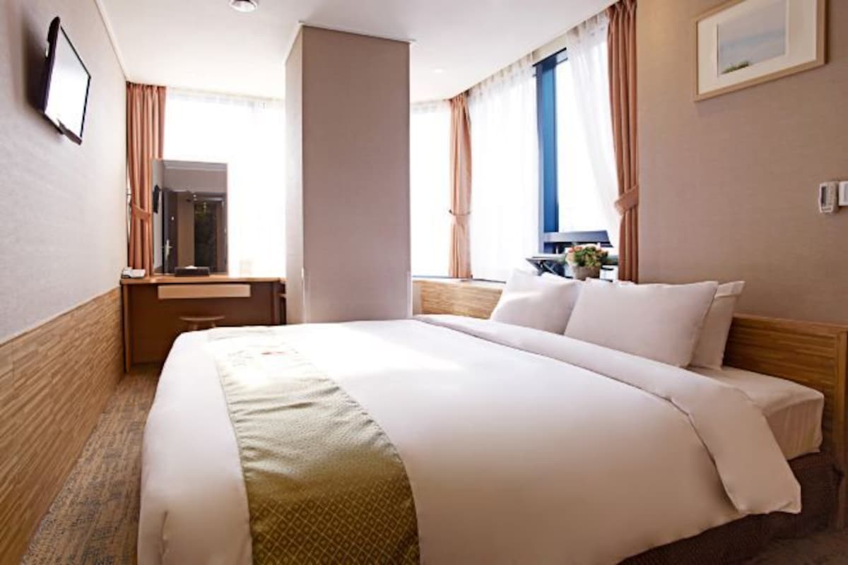 A hotel room with a large bed, a desk, and a window with curtains.