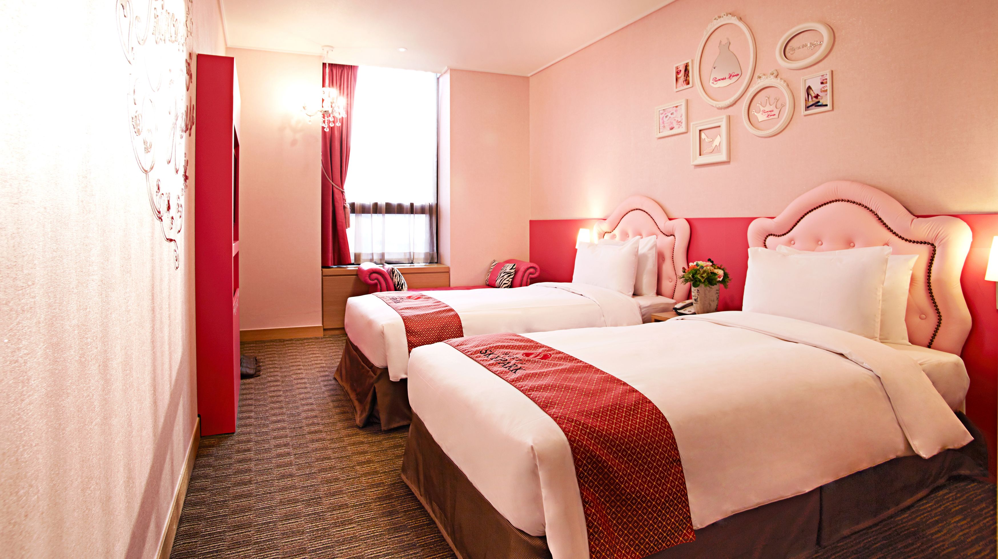 A hotel room with two beds, a red curtain, a chandelier, and wall decorations.