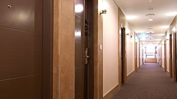 Un pasillo de hotel con suelo alfombrado, puertas a ambos lados y una lámpara en la pared.