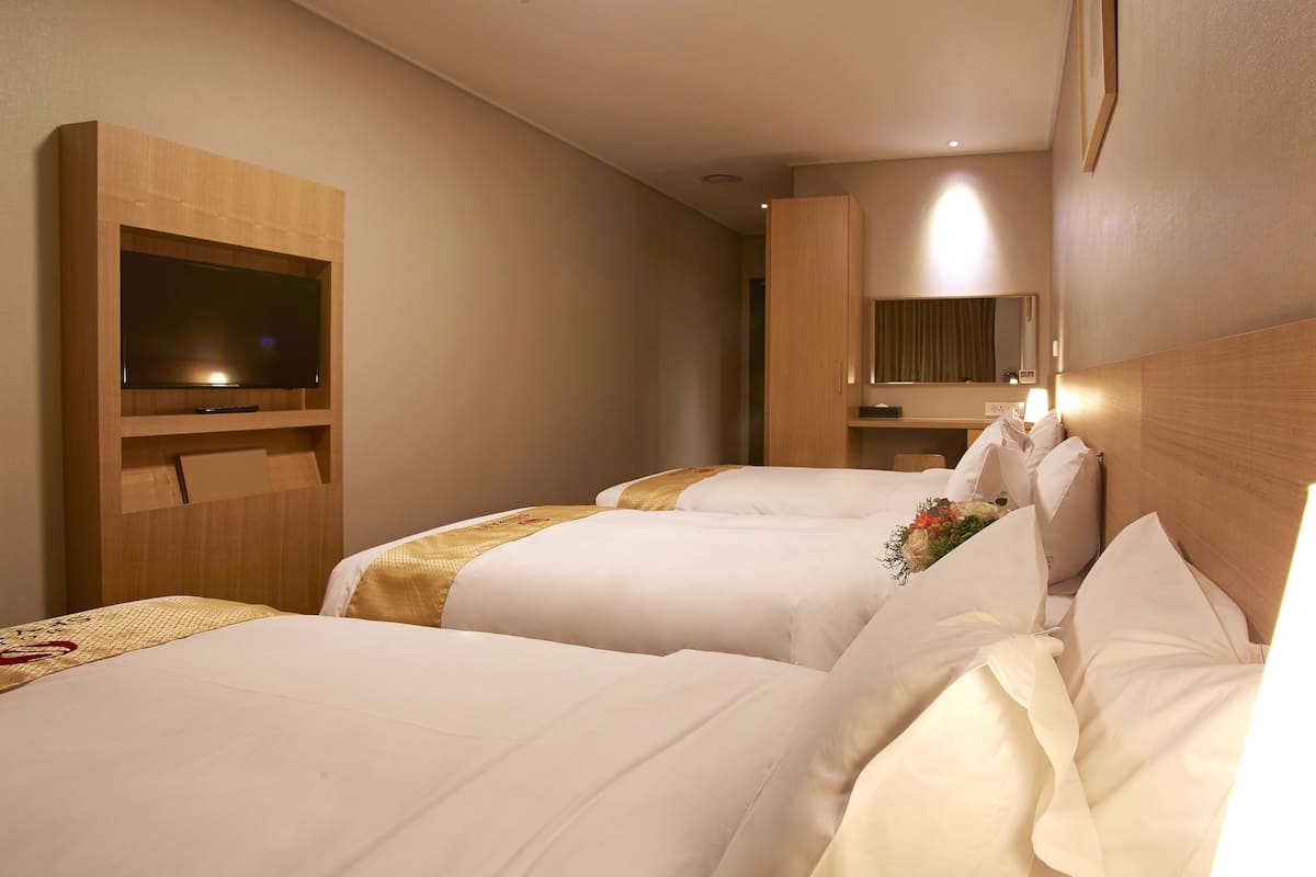 Et hotelværelse med to senge, et fjernsyn, et skrivebord og et spejl.