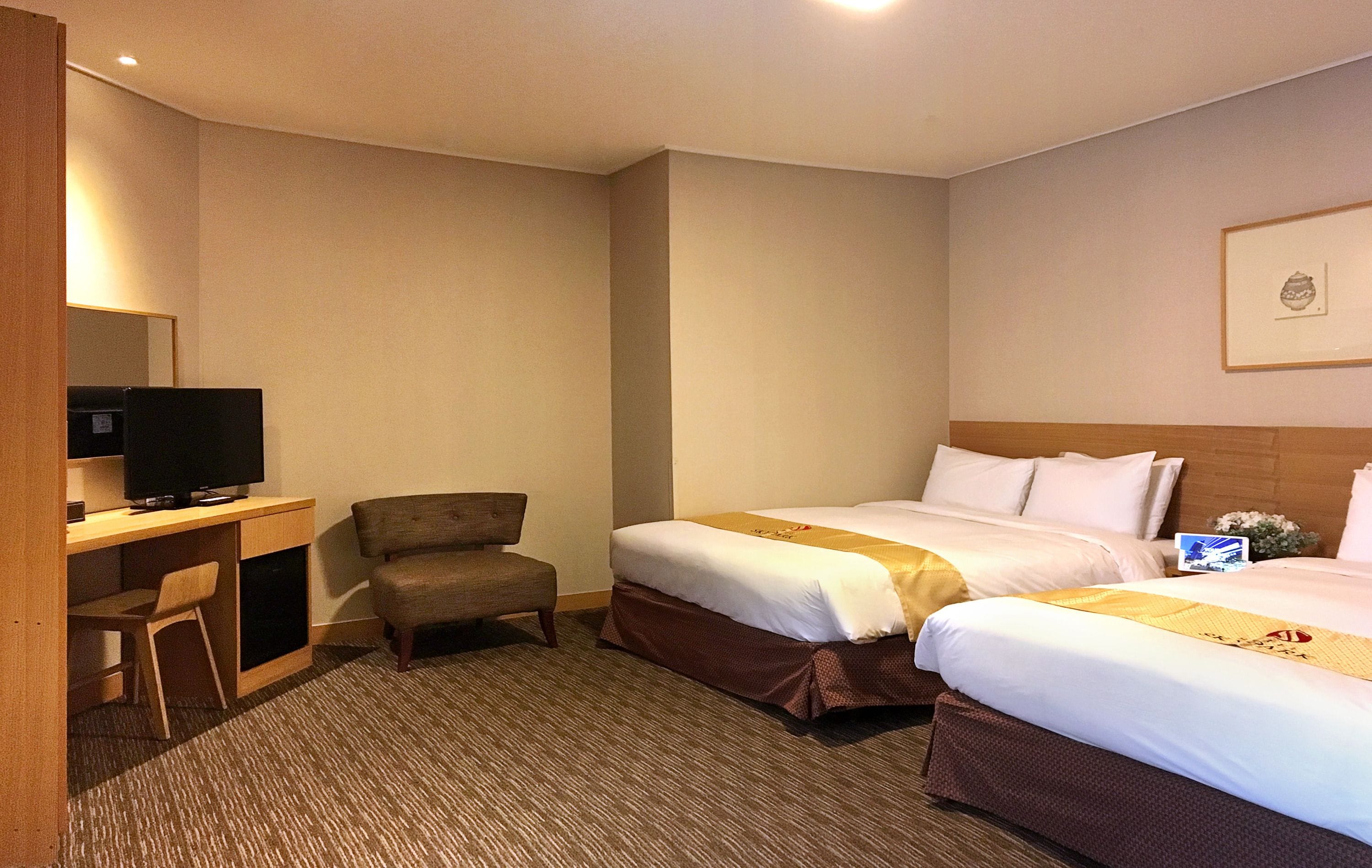 A hotel room with two beds, a desk with a television, and a chair.