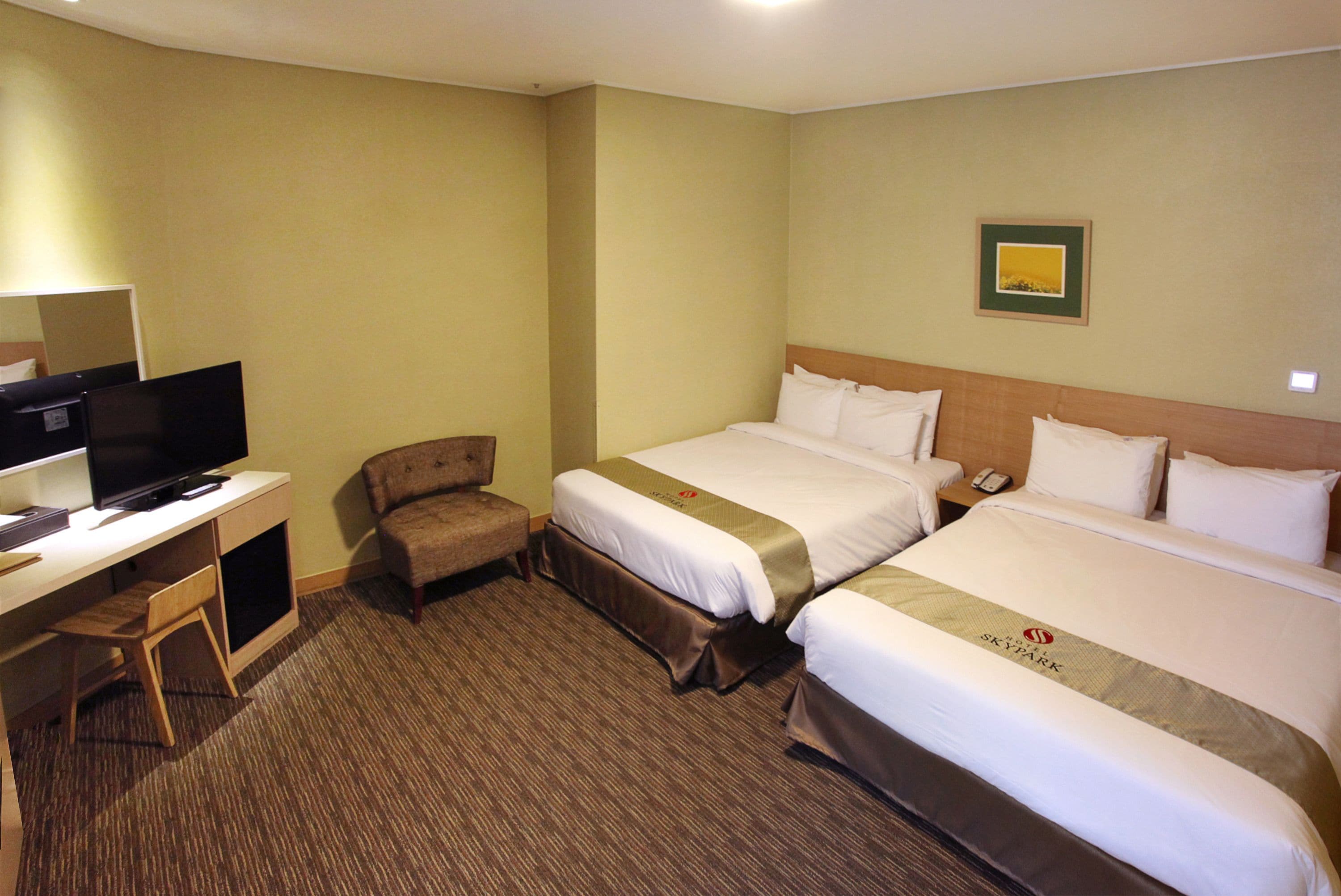 A hotel room with two beds, a desk with a television, and a small chair.